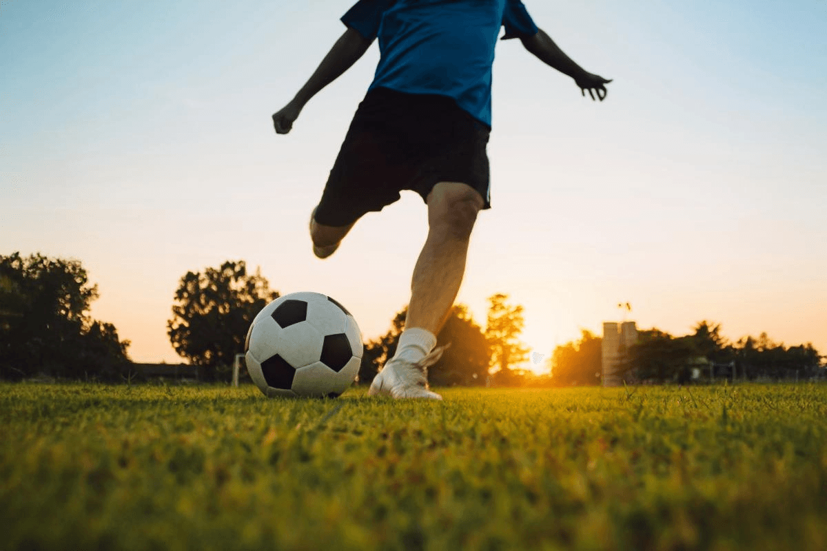 Soccer player kicking ball at sunset